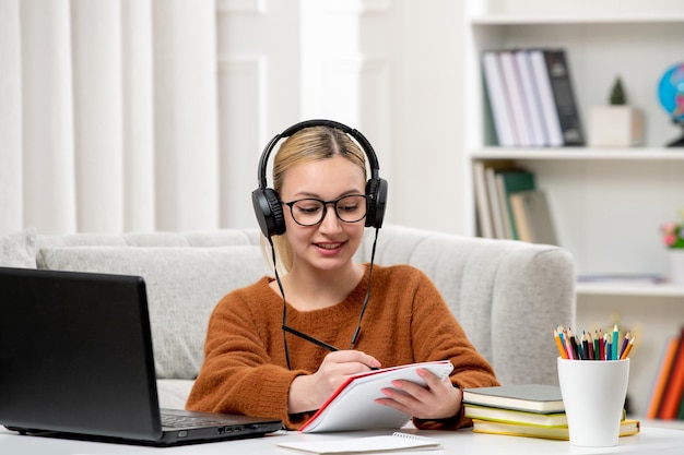 Student online cute girl in glasses and sweater studying on computer writing notes