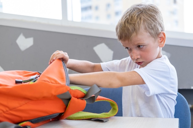 The student takes out stationery books from a backpack A little boy looks into a school bag Back to school School and preschool education