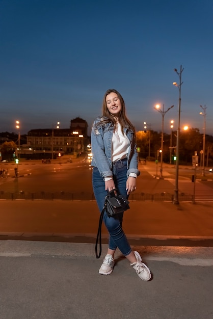 Student walks around the evening city. Beautiful girl posing on the street. Youth clothes. Vertical frame.