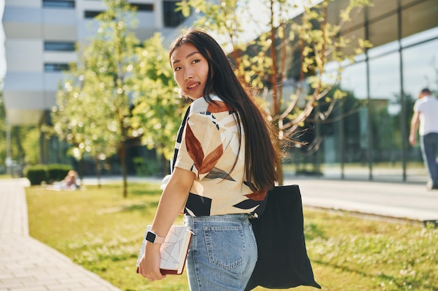 Student walks near modern building Young asian woman is outdoors at daytime