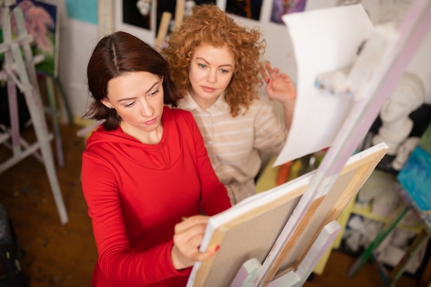 Student watching. Curly red-haired student feeling excited while watching her art teacher drawing