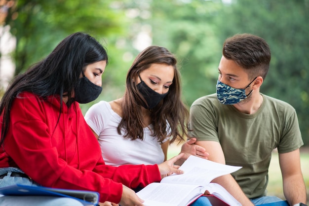 Students studying together sitting on a bench outdoor and wearing masks during coronavirus times