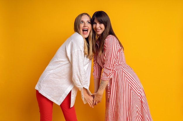 Studio bright positive portrait of two sisters woman having fun, color matching clothes, yellow  background. Cute emotions.