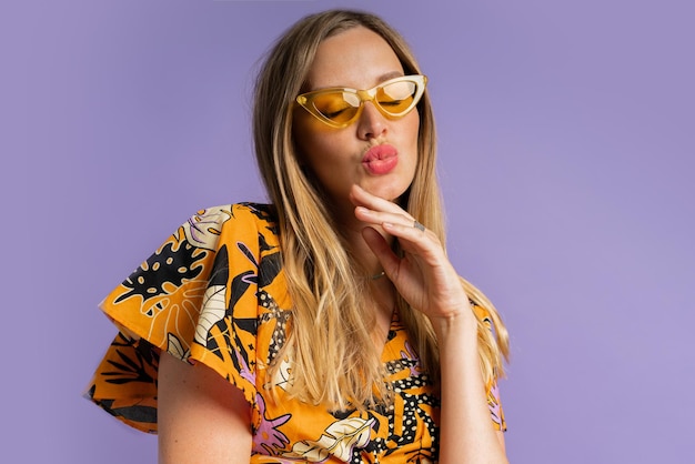 Studio close up fashion portrait of pretty blond woman in stylish top and linen shorts posing on purple background