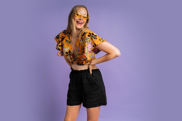 Studio fashion photo of pretty blond woman in stylish top and  linen shorts posing on purple background