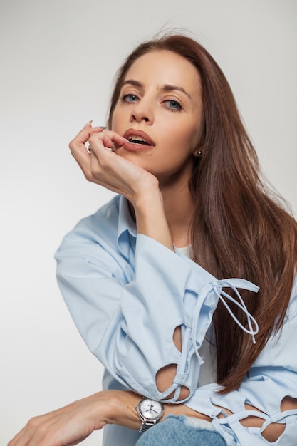 Studio fashion portrait of a beautiful sexy woman with healthy hair in fashionable denim casual clothes with a shirt sits looks at the camera and poses on a white background Pretty girl