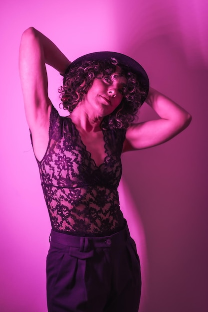 Studio lifestyle portrait of a young Caucasian woman with a beautiful outfit and a hat illuminated with a pink neon light