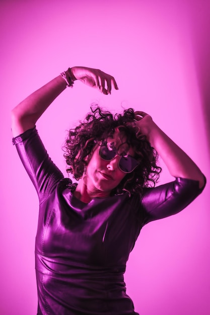 Studio lifestyle a young Caucasian woman having a lot of fun in a photo session with elegant clothes and sunglasses with neon pink light