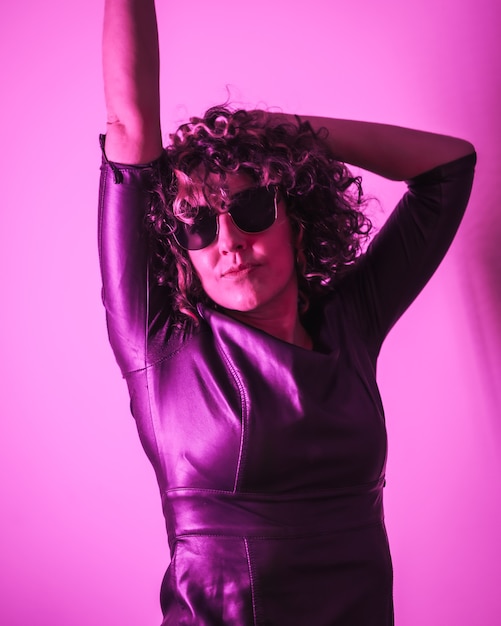 Studio lifestyle, a young Caucasian woman having a lot of fun in a photo session with elegant clothes and sunglasses, with neon pink light