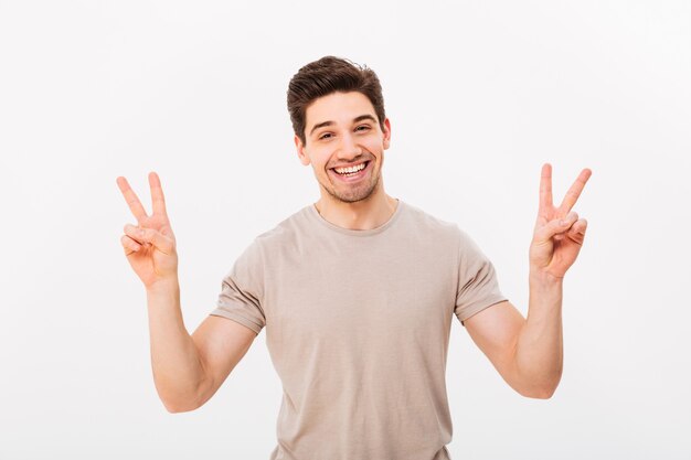 Photo studio photo of friendly guy model gesturing peace symbol with two hands and expressing gladness, isolated over white wall