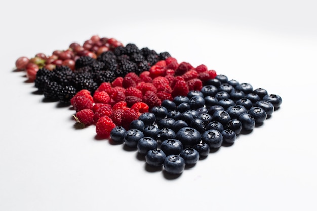 Studio picture of fresh wild berries situated in line, on the white table.