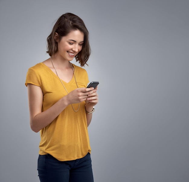 Studio portrait of an attractive young woman using her phone against a gray background