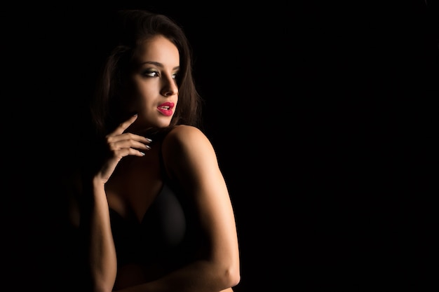 Studio portrait of attractive young woman with bright makeup posing with naked shoulders in the shadow