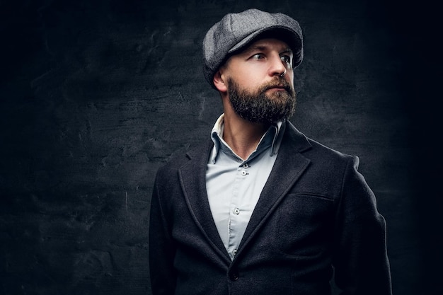 Photo studio portrait of bearded englishman in woolen hunting jacket and tweed cap.