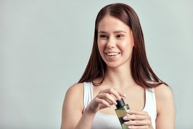 Studio portrait of beautiful smiling longhaired girl holding a bottle of cleansing lotion caucasian