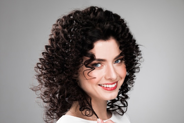 Studio portrait of beautiful smiling woman with curly dark hair on gray background