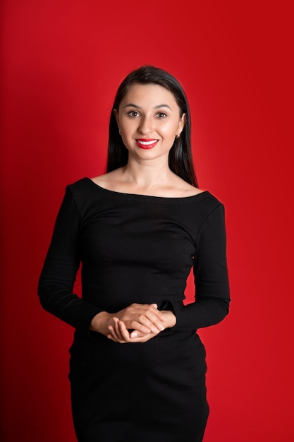 Studio Portrait of a Beautiful Young Woman in a Black Dress with Red Lipstick on Her Lips Red colored background