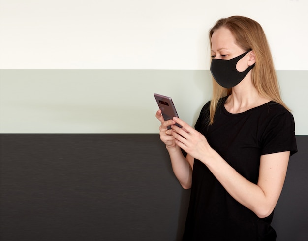 Studio portrait of blond woman in face mask with phone for protect during coronavirus epidemic.