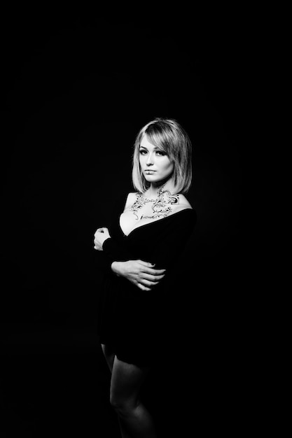 Studio portrait of blonde girl with originally make up on neck wear on black dress at dark background