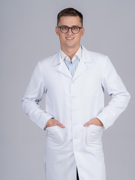 Studio portrait of a doctor or medical specialist. Standing with hands in pockets. Man in scrubs. Gray background.