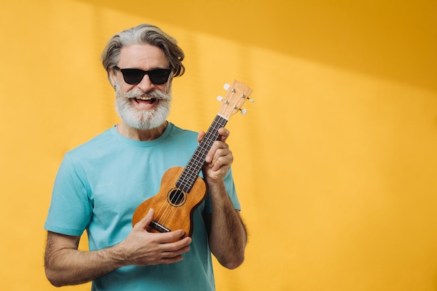 Studio portrait of an elderly man in sunglasses playing a ukulele