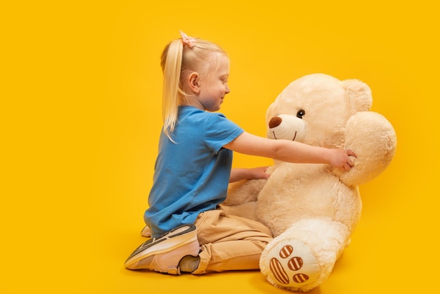 Studio portrait of little girl with large teddy bear on yellow background Child plays with soft toy