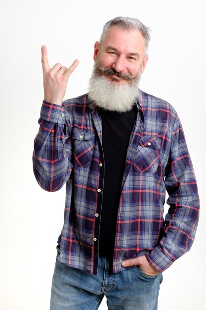 Studio portrait of mature bearded man in casual clothes showing horns up gesture