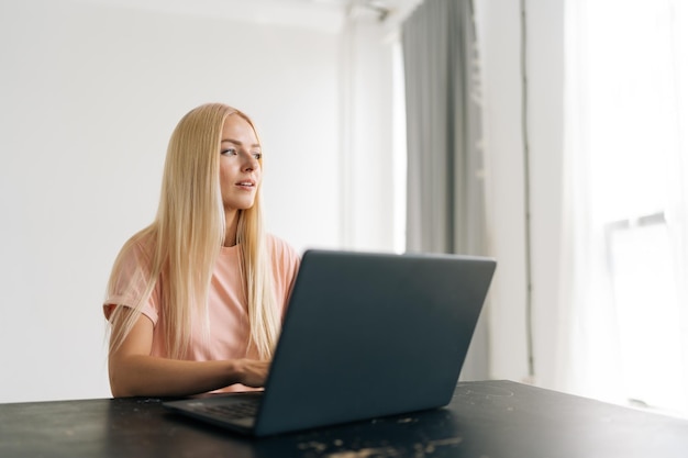 Studio portrait of pensive injured female freelancer with broken arm wrapped in white plaster bandage working typing on laptop computer looking away