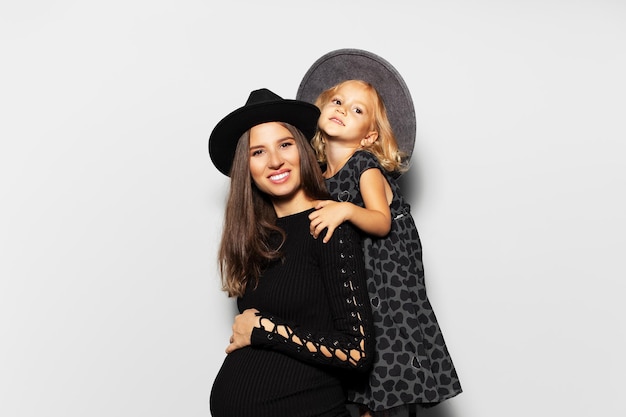 Studio portrait of pregnant happiness woman and child girl wearing hats on white background Mother and daughter in black