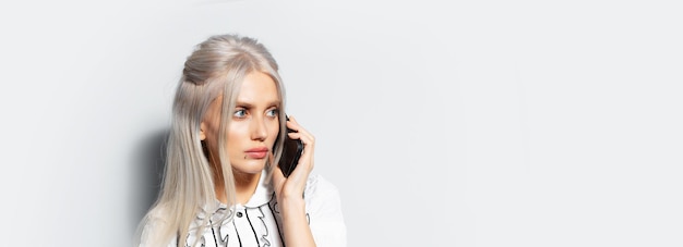 Studio portrait of pretty girl with blonde hair talking on smartphone wearing eyeglasses on white background panoramic banner view with copy space