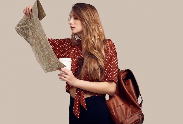 Studio portrait of pretty young hipster woman with backpack holding map