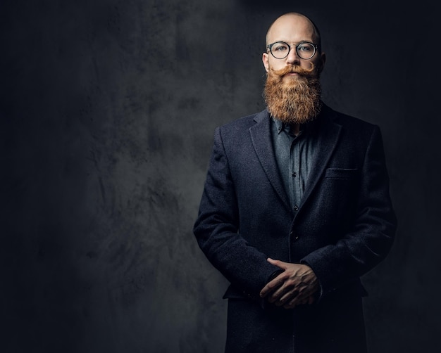 Studio portrait of redhead bearded male in vintage eyeglasses dressed in a wool jacket.