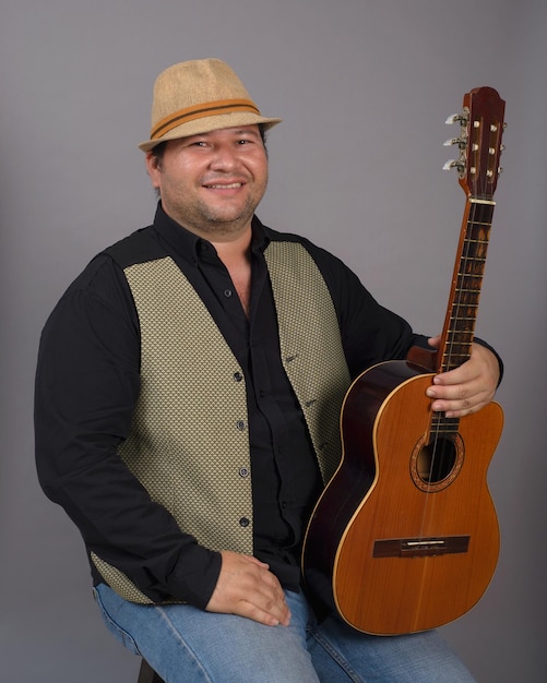 Studio portrait of seated man wearing hat and holding an old Cuban tres