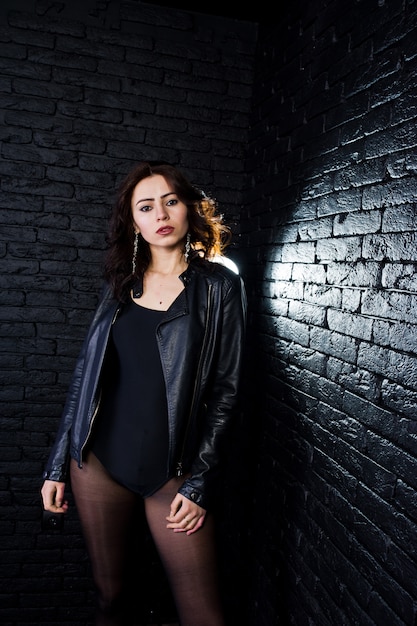 Studio portrait of sexy brunette girl in black leather jacket against brick wall.