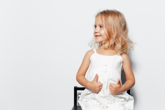 Studio portrait of smiling child girl with blonde hair on white background Showing thumbs up looking away Copy space concept