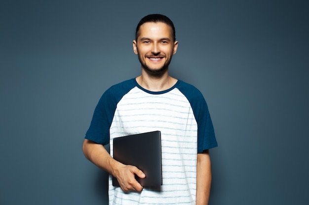 Studio portrait of smiling guy in shirt holding laptop on blue background