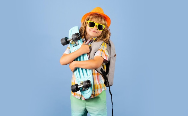 Studio portrait of stylish cute young child boy with skateboard isolated against blue background Kid