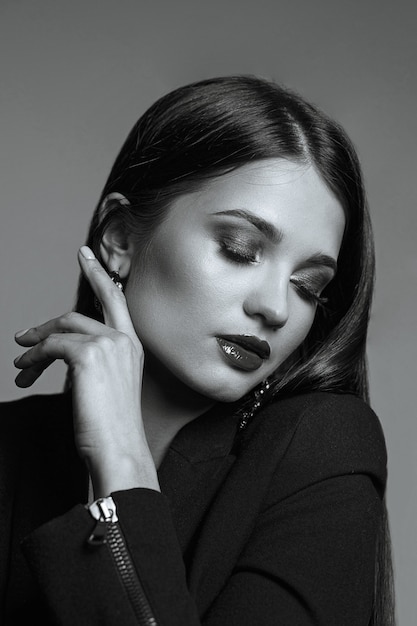 Studio portrait of tender woman with shiny brown hair and red lips wears silk dress posing with closed eyes. Black and white toning