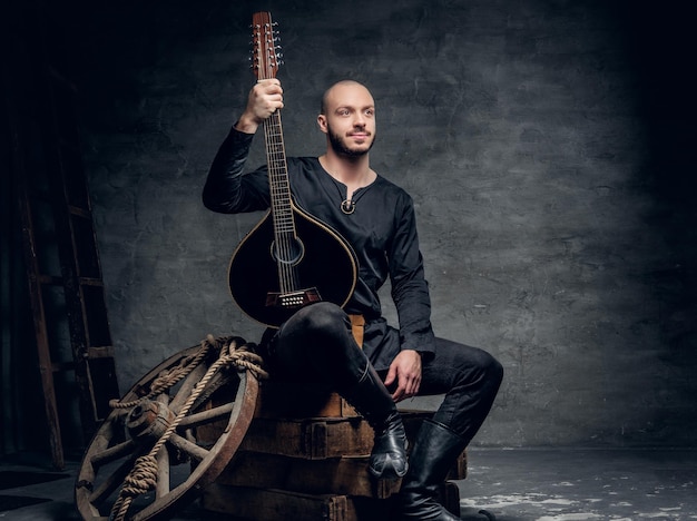 Studio portrait of traditional folk musician dressed in vintage Celtic clothes sits on a wooden box and holds mandolin.