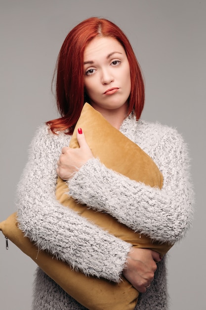 Studio portrait of a woman in a sweater hugging a pillow.