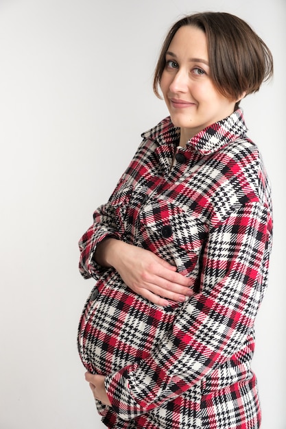 Studio portrait of young adult woman in warm home clothes, happy pregnancy concept, white wall