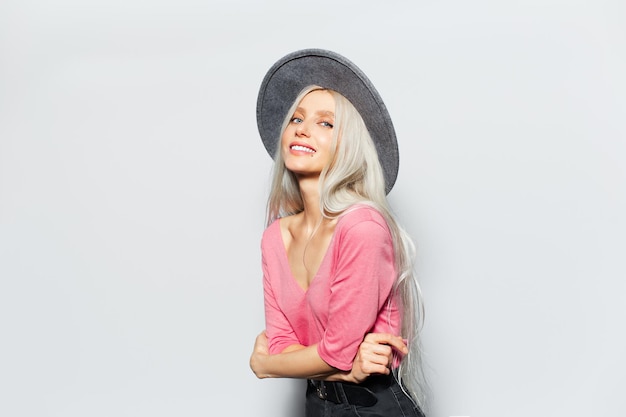 Studio portrait of young beautiful smiling girl with blonde hair wearing grey hat and pastel pink shirt on white background