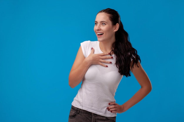 Studio portrait of a young beautiful woman in a white tshirt against a blue wall background people s...