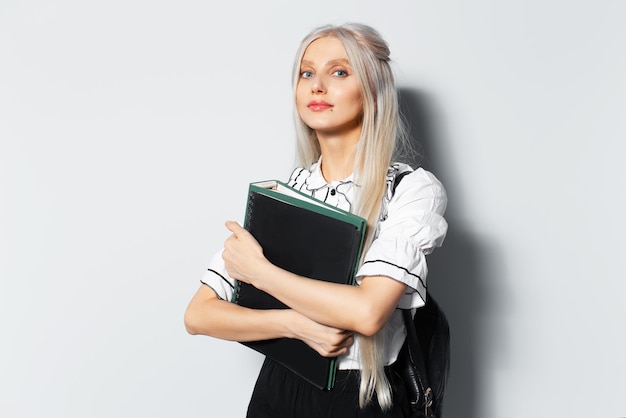 Studio portrait of young blonde beautiful girl holding a folders in hand wearing backpack on white background