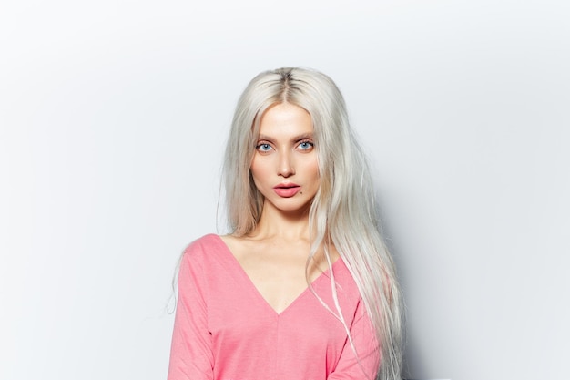 Studio portrait of young blonde pretty girl wearing pastel pink shirt on white background