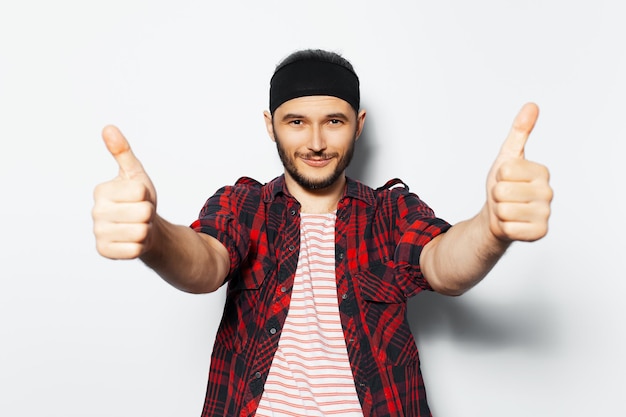 Studio portrait of young handsome man showing thumbs up on background of white wearing red casual clothes and black head band