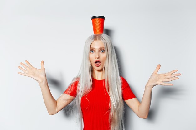 Studio portrait of young happiness blonde girl in red shirt holding paper cup for coffee takeaway on head on white background