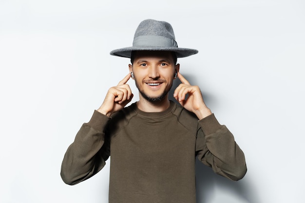 Studio portrait of young happiness man listening the music via wireless earbuds on white background wearing sweater and grey hat Touching earphones with fingers