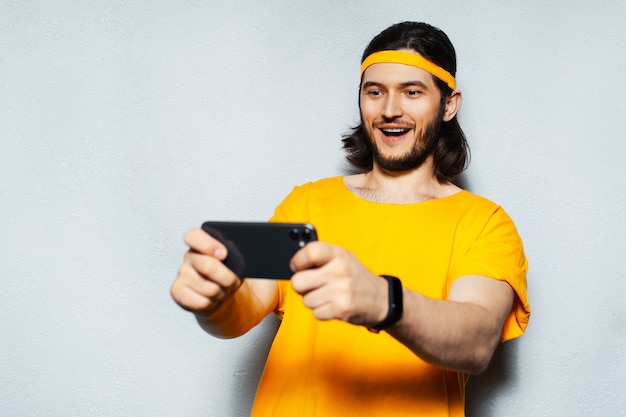 Studio portrait of young happy man using smartphone on grey textured background wearing yellow band for head and shirt.