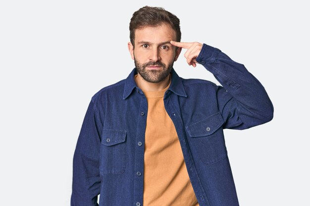 Photo studio portrait of young hispanic male pointing temple with finger thinking focused on a task